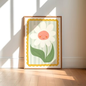 May include: A framed illustration of a white daisy with a smiling face, green leaves, and a yellow and green striped background. The frame has a yellow scalloped border.