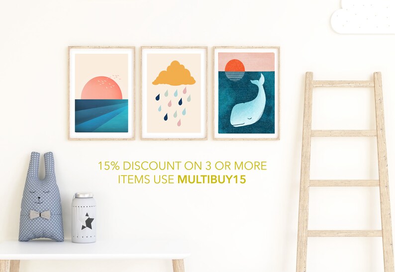 May include: Three framed prints with minimalist illustrations. The first print features a pink sunset over a blue ocean. The second print shows a yellow cloud with raindrops falling from it. The third print depicts a blue whale swimming under a setting sun. The text below the prints reads "15% DISCOUNT ON 3 OR MORE ITEMS USE MULTIBUY15".