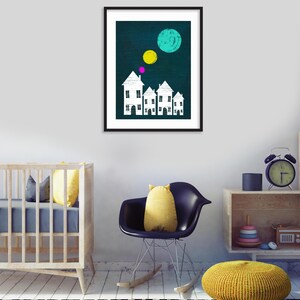 May include: A framed print with a dark blue background featuring white houses with pink and yellow circles above them. The houses are arranged in a row and have a simple design.