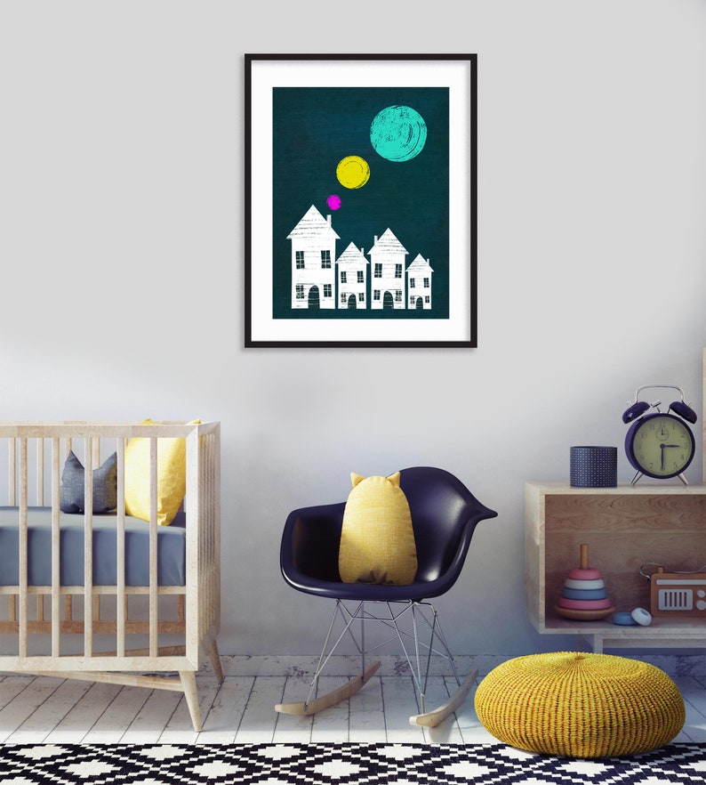 May include: A framed print with a dark blue background featuring white houses with pink and yellow circles above them. The houses are arranged in a row and have a simple design.