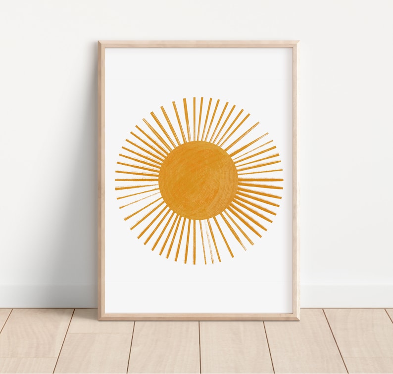 Op de afbeelding: Een ingelijste print van een gestileerde zon in geel-oranje. De zon heeft een cirkel in het midden met stralen die naar buiten uitstralen.
