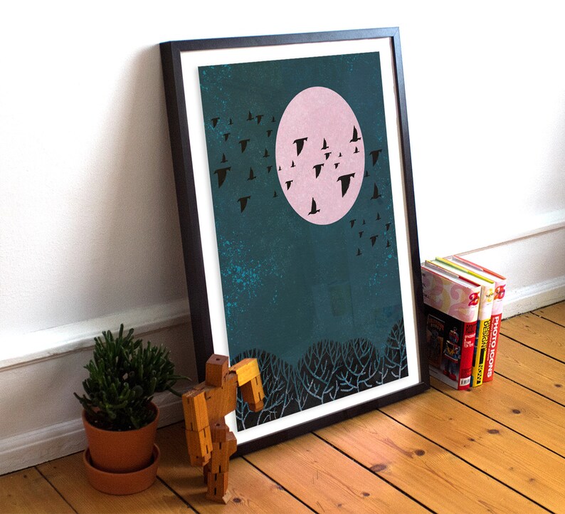May include: A framed print of a teal blue background with a pink moon and black silhouettes of birds flying in the sky. The print is in a black frame.