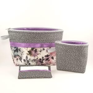 May include: Three gray and purple zippered pouches with white polka dots. The largest pouch has a floral print on the bottom half. The smallest pouch is a flat rectangle.