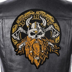 Könnte beinhalten: Eine schwarze Lederjacke mit einem großen gestickten Aufnäher auf der Rückseite. Der Aufnäher zeigt einen Schädel mit Bart und Hörnern, der einen Helm trägt und zwei Äxte hält. Der Schädel ist von einem kreisförmigen Design aus ineinander verschlungenen Knoten und Runen umgeben.