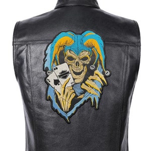 Puede incluir: Chaleco de cuero negro con un parche de calavera y cartas de juego de colores en la espalda. El parche presenta una calavera con un gorro de bufón y un diseño azul y amarillo.