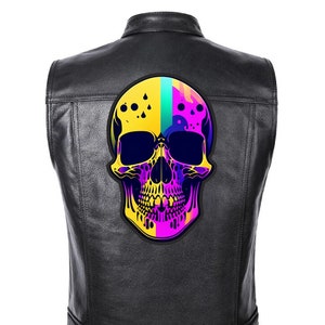 Può includere: Gilet in pelle nera con una toppa a forma di teschio colorato. Il teschio presenta tonalità gialle, blu, rosa e viola. Il gilet ha un classico stile biker con colletto e bottoni.