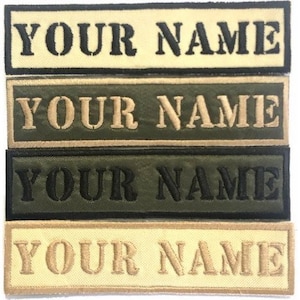 Puede incluir: Cuatro etiquetas bordadas con diferentes combinaciones de colores. Las etiquetas son beige con letras negras, verde con letras beige, verde con letras negras y beige con letras beige. Cada etiqueta dice "YOUR NAME".