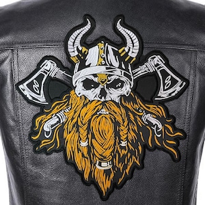 Peut inclure: Un patch brodé noir et blanc représentant un crâne de Viking avec un casque à cornes et une longue barbe tressée. Le crâne porte un casque avec un motif blanc et or. La barbe est d'un jaune vif. Le patch est entouré de deux haches avec des motifs blancs et or.