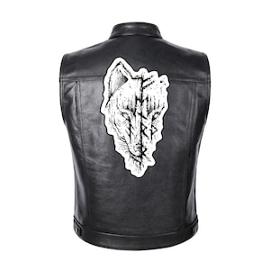Könnte beinhalten: Schwarze Lederweste mit einer weiß-schwarzen Wolfsgrafik auf dem Rücken. Das Wolfsdesign ist eine stilisierte Illustration mit einem verwitterten, strukturierten Aussehen. Die Weste hat einen klassischen Biker-Stil.