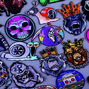 Op de afbeelding: Een verzameling kleurrijke geborduurde strijkpatches met verschillende ontwerpen, waaronder schedels, een slak, een grim reaper, een gorilla, een beer en een hond. De patches zijn perfect om kleding, tassen of andere accessoires een unieke touch te geven.
