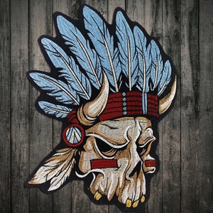 Op de afbeelding: Gestikt patch met een schedel die een blauwe en witte veren hoofdtooi draagt met een rood en wit hoofdband. De schedel heeft hoorns en een gedetailleerd ontwerp.