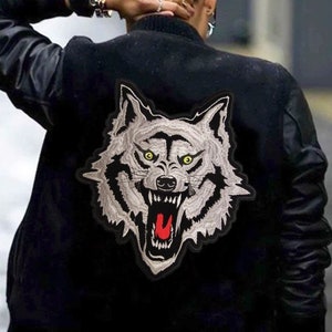 May include: A black bomber jacket with a large embroidered wolf head patch on the back. The wolf is gray with a red open mouth and yellow eyes.