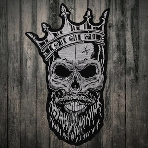 Può includere: Toppa ricamata in bianco e nero di uno scheletro con una corona e una barba.