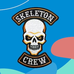 Può includere: Toppa ricamata con un teschio e le parole "SKELETON" e "CREW". Il teschio è bianco con dettagli gialli e neri. La toppa ha un bordo nero con cuciture gialle.