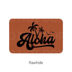 May include: A rectangular, rawhide-colored item with rounded corners. The word "Aloha" is written in a black, stylized font, with palm trees and birds above the text. The word "Rawhide" is written below the main design.
