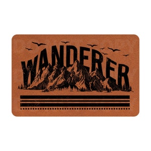 May include: A brown leather-like doormat with the word "WANDERER" in black lettering. The word is stylized with a mountain range behind it and birds flying above.