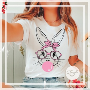 May include: White t-shirt with a graphic of a cartoon bunny wearing pink heart-shaped glasses and a pink polka dot headband. The bunny is blowing a pink bubble.