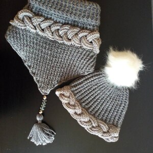 May include: Gray knitted hat and scarf set with a white pom pom on the hat and a gray tassel on the scarf.