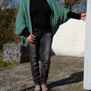 May include: A green crocheted cardigan with a loose fit and long sleeves. The cardigan is open in the front and has a simple, elegant design.