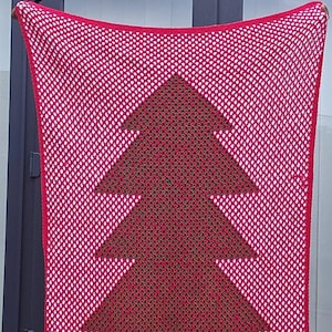 May include: A red and white crocheted blanket featuring a Christmas tree design in the center. The tree is a darker shade of red. The blanket is held up in front of a door.