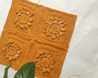 May include: Four crocheted squares in a mustard yellow color, joined together to form a larger square. Each square features a detailed floral design in the center.