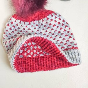 May include: A red and gray crocheted beanie with a burgundy pom pom.