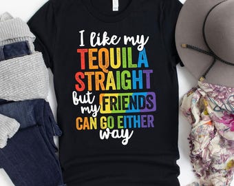 May include: Black t-shirt with the text "I like my TEQUILA STRAIGHT but my FRIENDS can go either way" in rainbow colors. The shirt is displayed with a gray hat, scarf, and folded jeans.