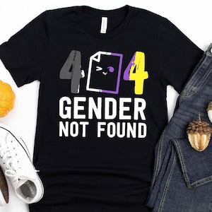 May include: Black t-shirt with the text "404 GENDER NOT FOUND". The design includes the numbers 4 in gray and yellow, a document icon with a purple border, and the text in white. The shirt is paired with blue jeans and white sneakers.