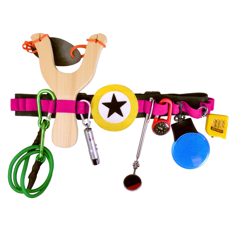May include: A pink and black utility belt with a variety of tools and accessories, including a slingshot, a compass, a whistle, a mirror, a flashlight, and a green bungee cord.