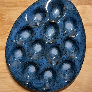May include: A blue ceramic egg-shaped serving dish with 12 individual indentations for holding eggs or other small snacks.