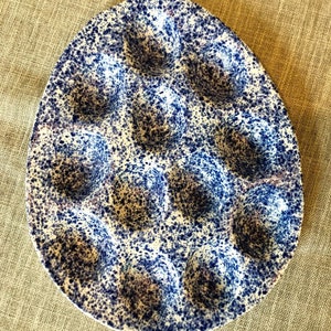 May include: A white ceramic egg holder with a blue speckled pattern. The holder has eight individual indentations for eggs.
