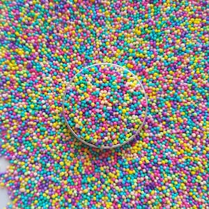 May include: A close-up of a silver bowl filled with colourful sprinkles. The sprinkles are a mix of pink, blue, yellow, green, and purple.