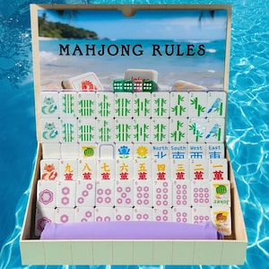 May include: A Mahjong set in a wooden box with a lid featuring a beach scene and the text MAHJONG RULES. The set includes white tiles with green bamboo, red and black Chinese characters, floral patterns, and colourful bird and dragon icons.