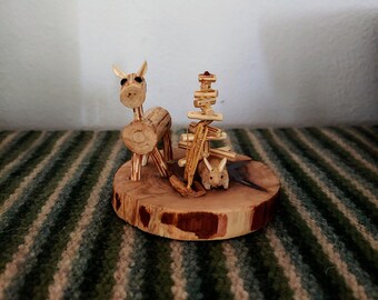 May include: A wooden figurine set featuring a deer, a tree, and a small rabbit. The figurines are made of natural wood and have a rustic, handcrafted look.