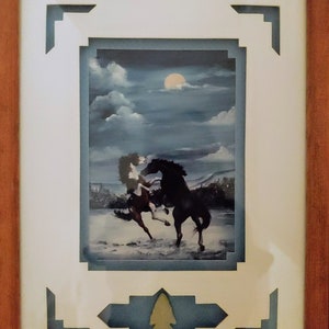 May include: Framed artwork featuring a painting of two horses running in a snowy landscape under a full moon. The frame has a blue and white border with a decorative arrowhead design.