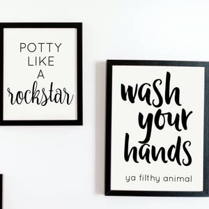 May include: Two framed wall art prints with black frames. One print reads "Potty Like A Rockstar" in black script. The other print says "Wash Your Hands ya filthy animal" in black script.