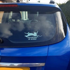 Peut inclure: Une voiture bleue avec un autocollant blanc sur la vitre arri&egrave;re qui dit "Greyhound on Board". L'autocollant repr&eacute;sente une silhouette de l&eacute;vrier courant.