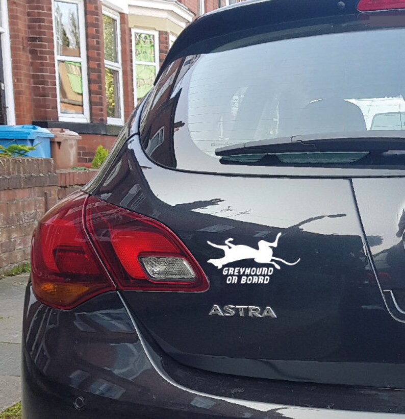 Peut inclure: Une voiture noire avec un autocollant blanc qui dit "Greyhound on Board" et une silhouette blanche d'un l&eacute;vrier courant. La voiture est une Opel Astra.