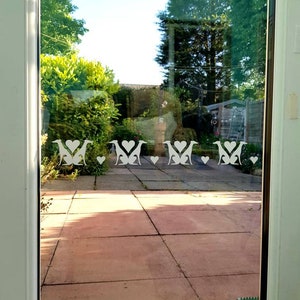 May include: White vinyl window decals of dogs with hearts. The decals are on a glass door with a view of a backyard.