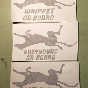 Peut inclure: Trois autocollants blancs avec des silhouettes grises de chiens et le texte "Whippet on board", "Greyhound on board", et "Lurcher on board".