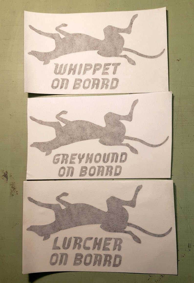 Peut inclure: Trois autocollants blancs avec des silhouettes grises de chiens et le texte "Whippet on board", "Greyhound on board", et "Lurcher on board".