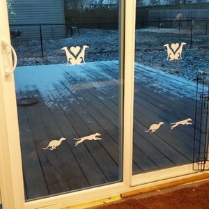 Puede incluir: Una puerta de vidrio con una silueta blanca de dos perros corriendo y una silueta blanca de dos perros con un coraz&oacute;n en el medio. La puerta est&aacute; abierta y muestra una terraza de madera con nieve.