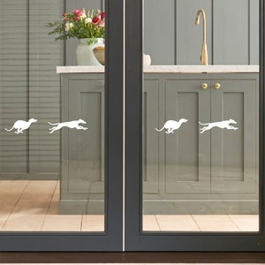 Puede incluir: Cuatro calcoman&iacute;as de silueta blanca de galgos corriendo, aplicadas a una puerta de vidrio con vista a una cocina. La cocina tiene gabinetes grises y un fregadero de acero inoxidable.