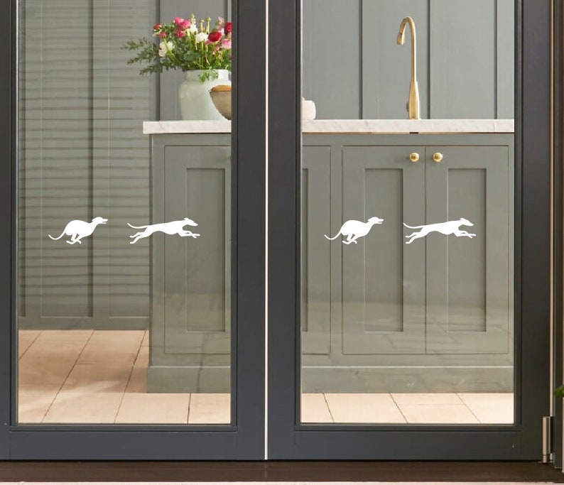 Puede incluir: Cuatro calcoman&iacute;as de silueta blanca de galgos corriendo, aplicadas a una puerta de vidrio con vista a una cocina. La cocina tiene gabinetes grises y un fregadero de acero inoxidable.