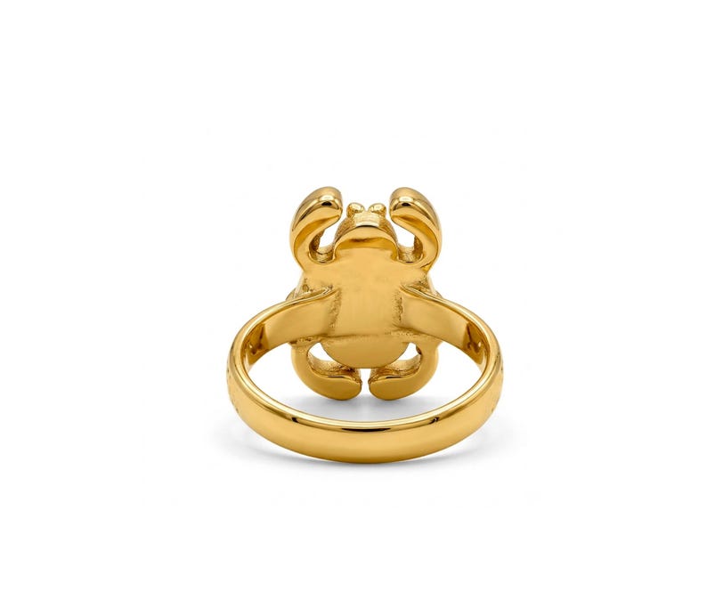 May include: A gold-toned ring featuring a stylised crab design on the face. The band is smooth and circular, while the crab motif displays rounded pincers and legs extending from the central body. The entire piece has a polished, reflective finish.