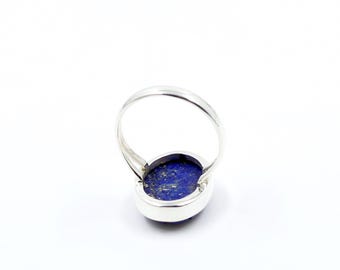 May include: A silver ring with a large, oval lapis lazuli stone. The deep blue stone, flecked with gold, is set in a polished silver band. The ring is displayed against a white background.