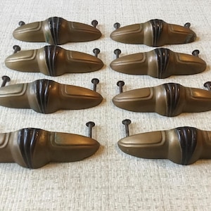 Könnte beinhalten: Acht antike Messing-Schubladengriffe mit schwarzen Akzenten. Die Griffe sind tropfenförmig mit einer abgerundeten Oberseite und einer flachen Unterseite. Sie haben einen Vintage-Look und wären perfekt, um jedem Zuhause einen Hauch von Eleganz zu verleihen.