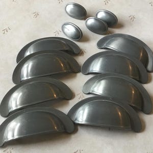 以下が含まれることがあります： 半円形のシルバー調の金属製のキャビネット引き出しプルが10個。プルは2列5個ずつ配置されています。