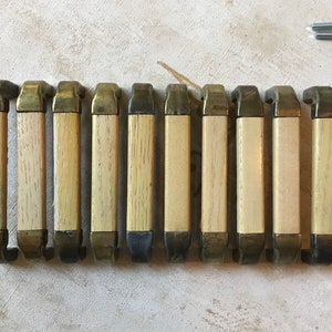 以下が含まれることがあります： 真鍮と黒色の金属のアクセントが付いた木製のキャビネットノブが10個。ノブはすべて同じサイズと形であり、長方形のデザインです。