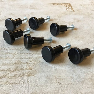 May include: Eight black ceramic cabinet knobs with silver screws. The knobs are round and have a smooth, glossy finish.